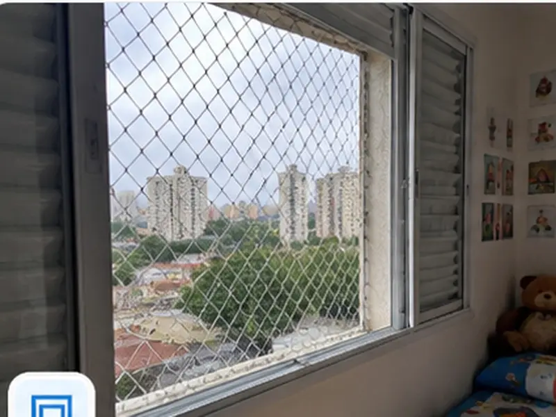 Mãe e filha em um quarto observando a vista por uma janela com rede de proteção instalada